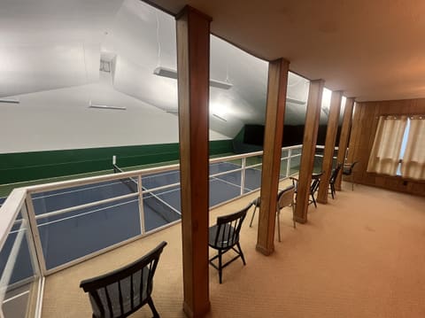 The Court 1 viewing balcony: chairs along a railing above the court, with wood-panelled walls and curtained windows.