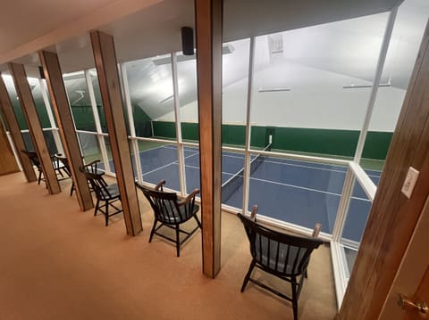 The Court 2 viewing balcony: wooden chairs lined up at tall windows looking down on the blue court.
