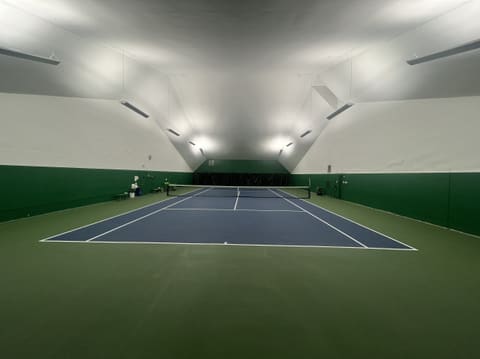 Court 3 seen from behind the baseline: a blue court with a wide green surround and bright ceiling lights.