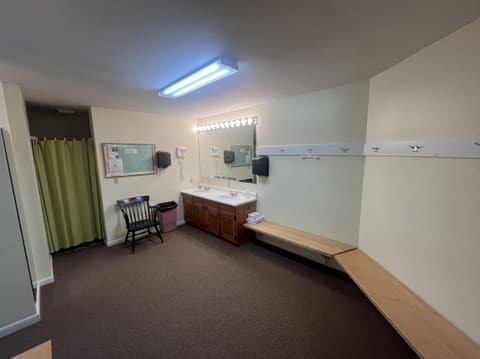 The ladies' locker room: a double sink with a lit mirror, wooden benches, coat hooks and a curtained shower.