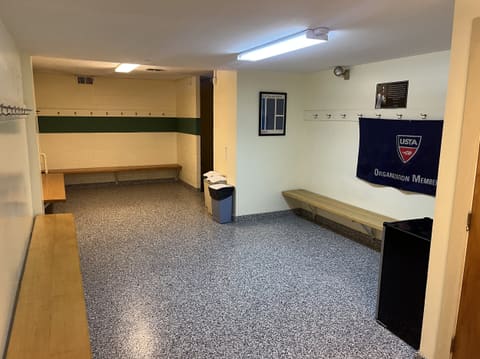 The men's locker room: wooden benches, coat hooks and a USTA Organization Member banner on the wall.